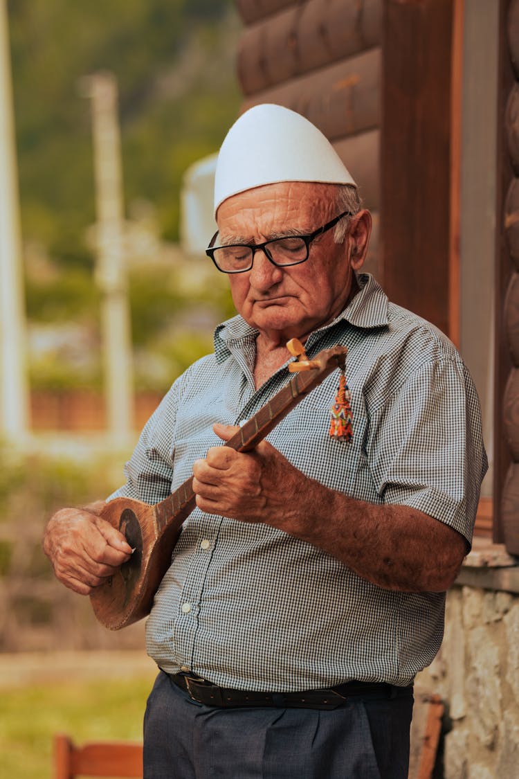 Man Wearing White Kufi Cap Standing While Playing Ukelele