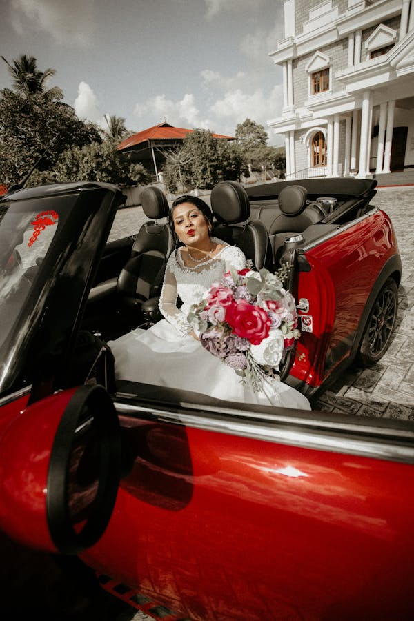 Woman in White Wedding Gown Sitting on Red and White Convertible Car