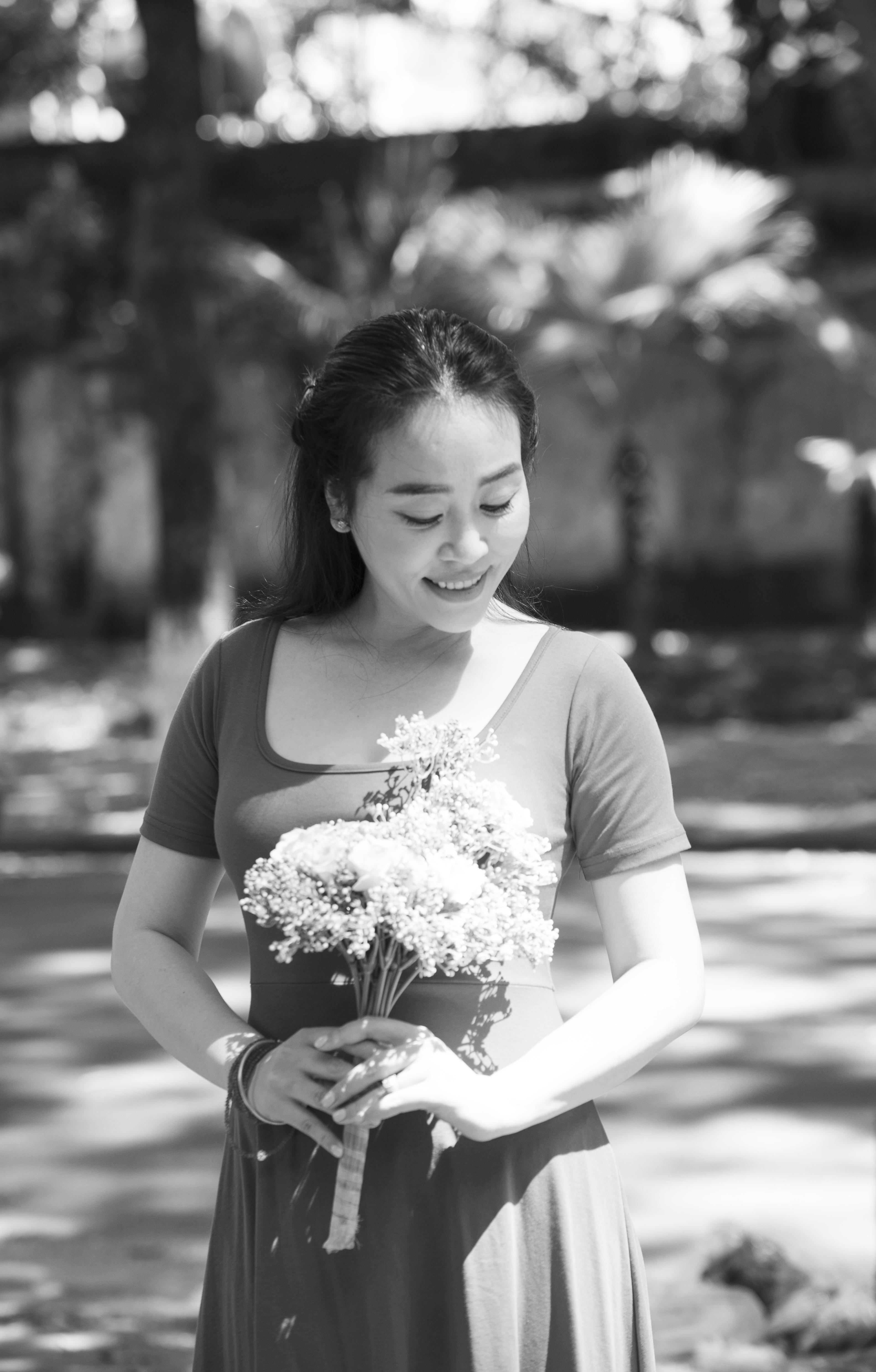Smiling woman holding a flower bouquet in a sunlit outdoor setting.