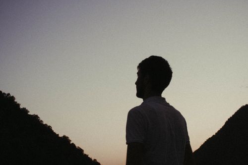 Free Silhouette of a man against twilight sky, framed by mountains, creating a serene and contemplative atmosphere. Stock Photo