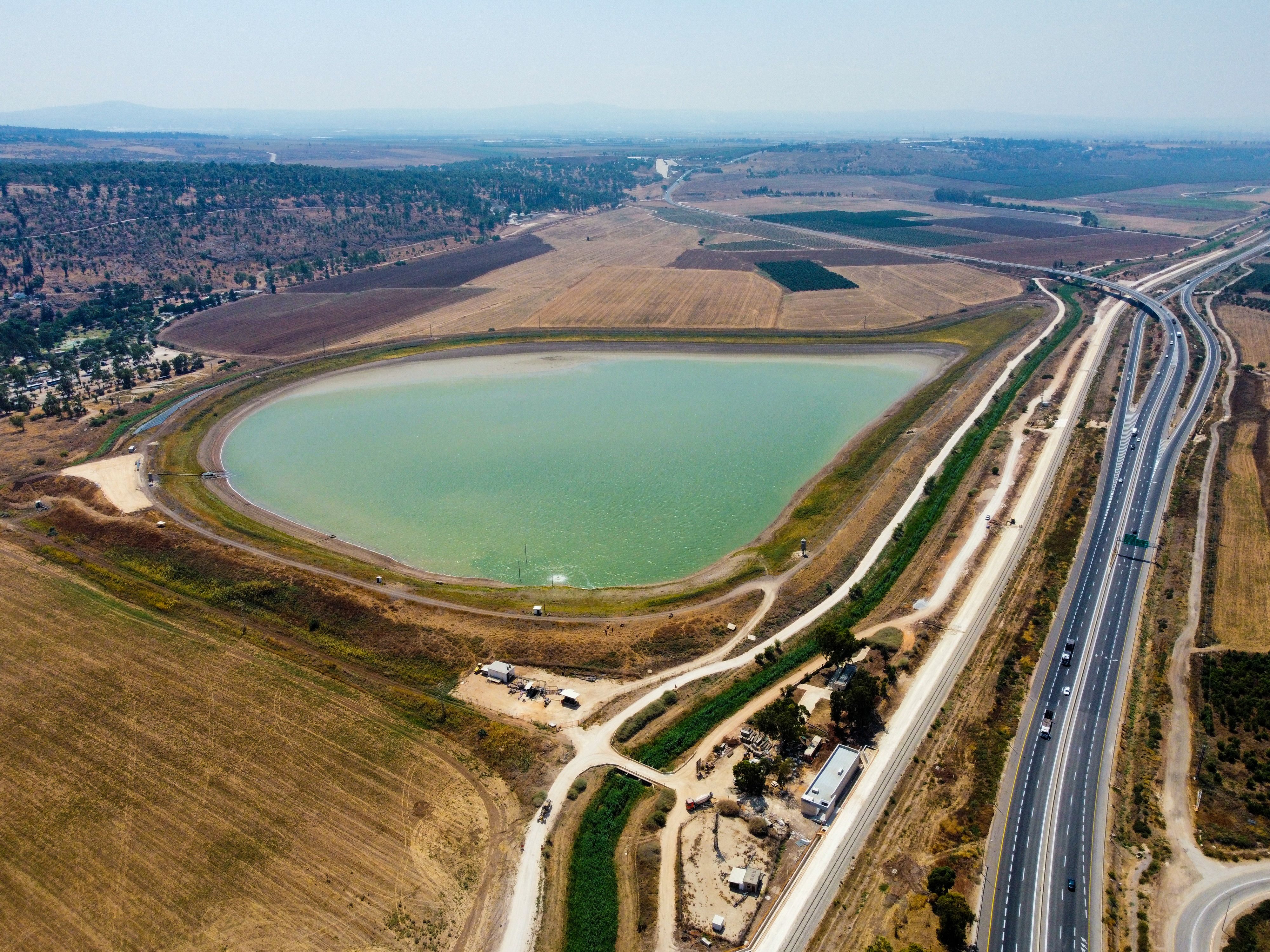 Drone shot of a rural landscape featuring a body of water, fields, and transportation routes.