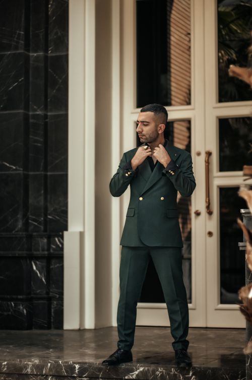 Free A fashionable man in a green suit adjusts his collar outside a luxurious building. Stock Photo