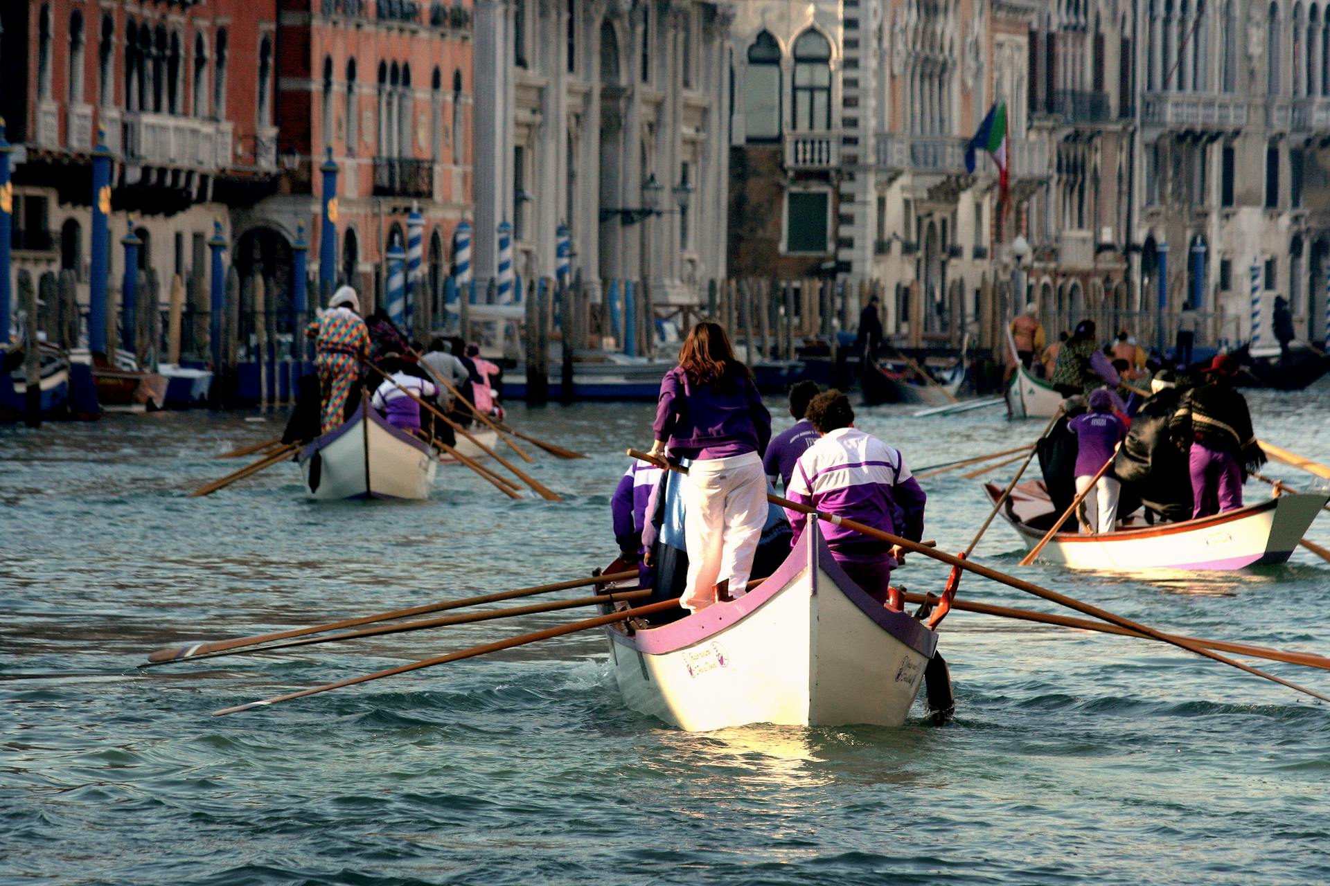 Boats racing in Venice's Grand Canal during a festive rowing event with vibrant costumes.