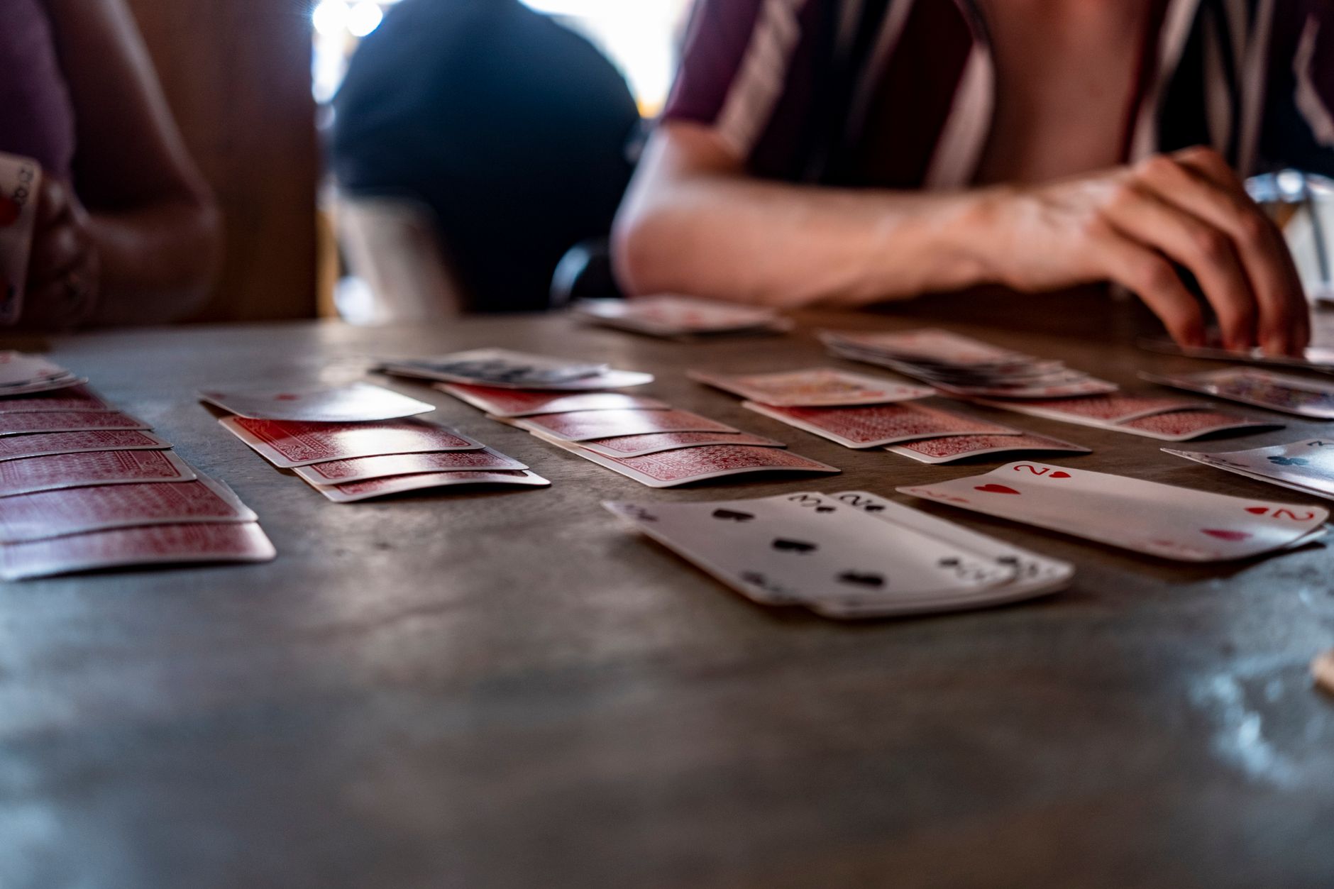 Intimate tabletop scene of people playing cards with a focus on hands and playing cards.