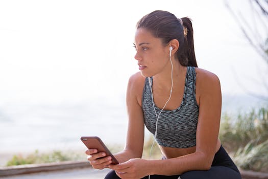 一位健康的女性戴着耳机和智能手机，在户外锻炼期间休息