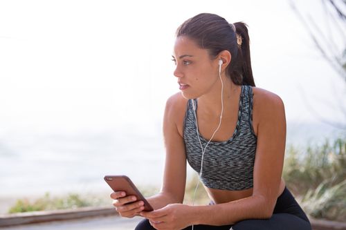 Free Fit woman with earphones and smartphone taking a break during an outdoor workout. Stock Photo