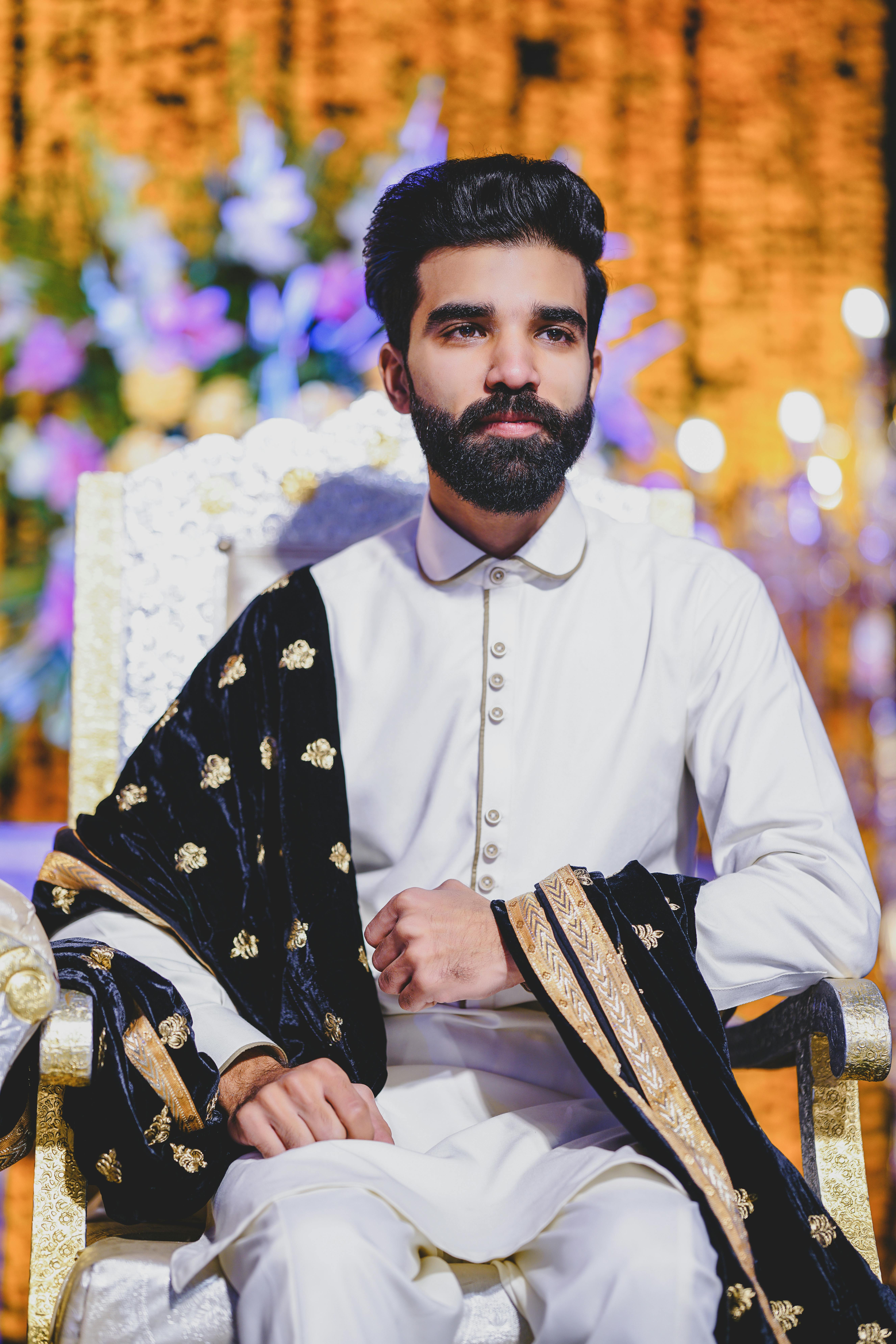 Elegant portrait of a man in traditional attire sitting on an ornate chair with a vibrant background.