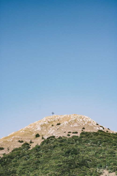 Free A tranquil mountain peak topped with a cross under a vast blue sky, offering peaceful solitude. Stock Photo