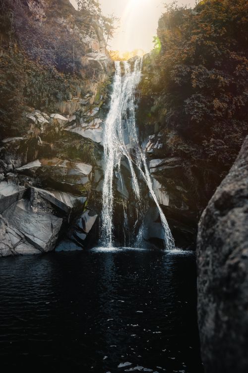 Free A serene waterfall flowing over rocky cliffs surrounded by lush vegetation. Stock Photo