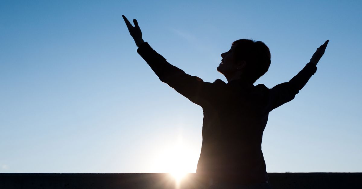 person looking at a sunrise with hands slightly raised, peaceful expression