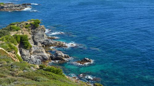 Free Breathtaking view of rocky coastline with lush greenery and vibrant blue sea. Stock Photo