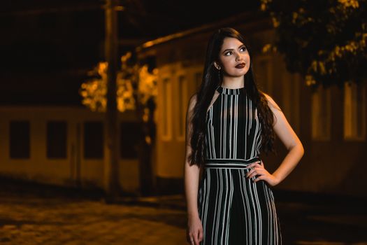 Stylish woman in a striped dress poses confidently outdoors at night, showcasing urban elegance.