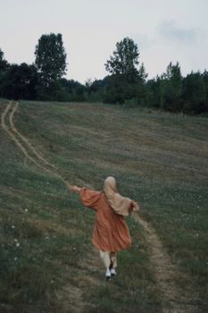 A woman in a headscarf enjoying a peaceful walk in a grassy countryside field.