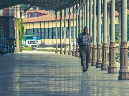 A Man in Blue and White Plaid Shirt Walking Near Columns