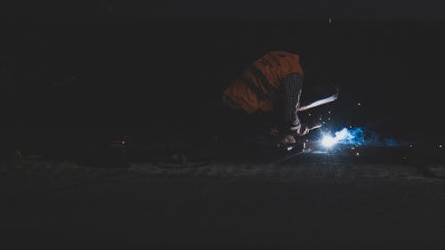 A Person in Orange Vest Welding in a Dark Place