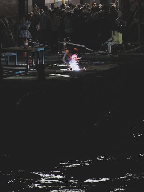 A Person Welding Near a Crowd during Night Time