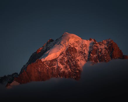 Beautiful dusk view of a majestic snow-covered mountain peak with warm golden sunlight casting over it.