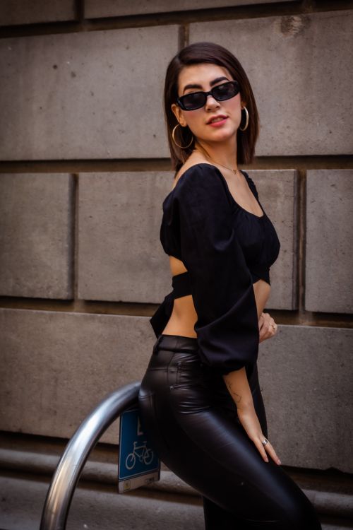 Free Chic woman wearing black attire and sunglasses leans confidently against urban backdrop. Stock Photo