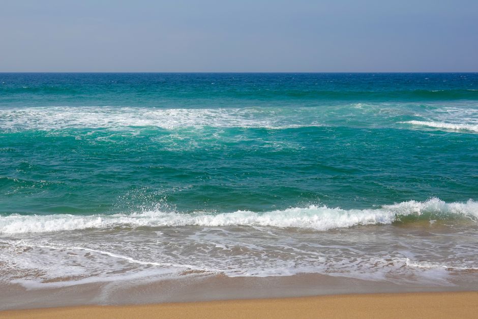 Enjoy the serene beauty of turquoise waves crashing on a sandy beach under a clear sky.
