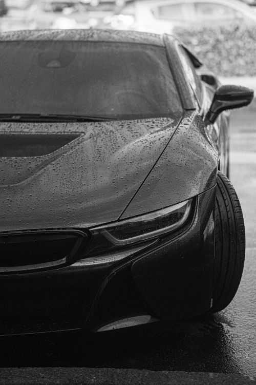 Free Black sports car parked on a wet road, detailed headlight view in grayscale. Stock Photo