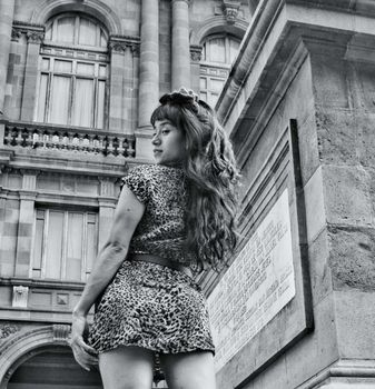 Grayscale portrait of a woman in stylish dress posing outdoors in front of historic building.