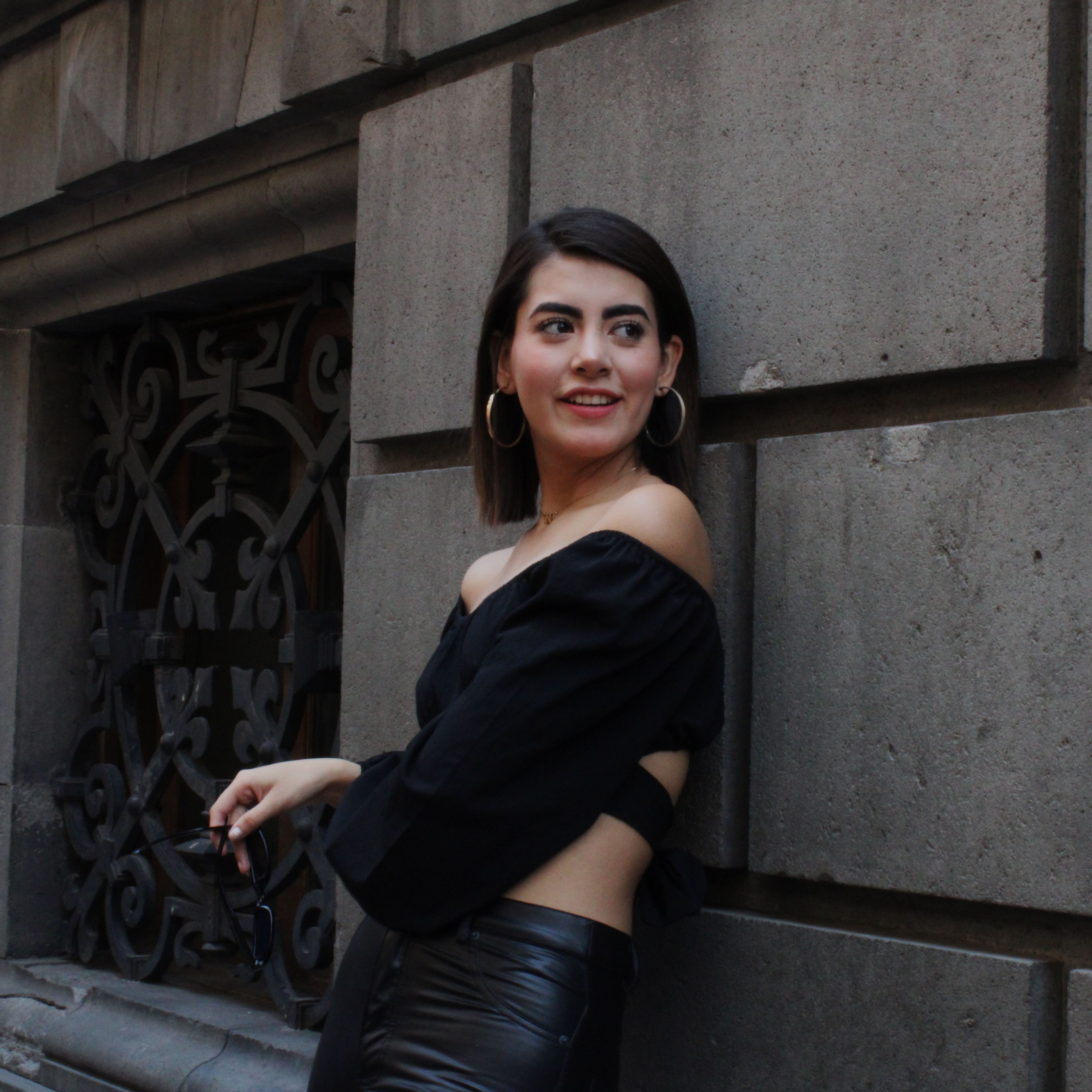 A fashionable woman posing against a classical building's stone wall during the day.