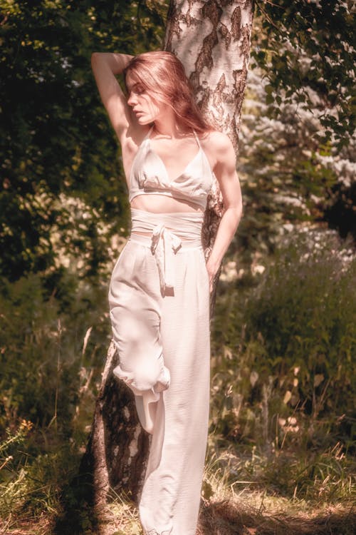 Young Woman Posing in White Halter Crop Top Leaning on a Tree Trunk