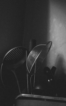 A black and white photograph of various kitchen utensils with dramatic shadows, creating a moody atmosphere.