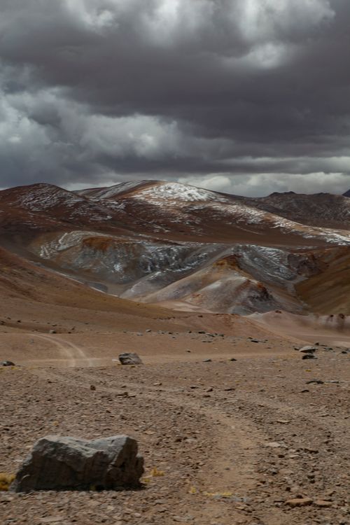 Free Rugged desert terrain with dramatic cloud formations and distant mountain view. Stock Photo