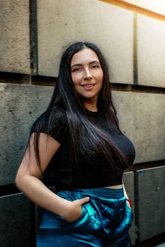 A young woman smiles confidently while posing against a concrete wall in an urban setting.