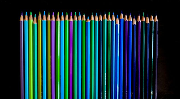 Vibrant colored pencils arranged neatly on a black surface.