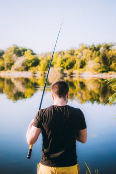 A man enjoys a peaceful day fishing by a reflective lake in summer, holding a fishing rod.