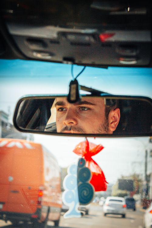 Free A man with facial hair focuses on the road, reflected in the rear view mirror of a vehicle. Stock Photo
