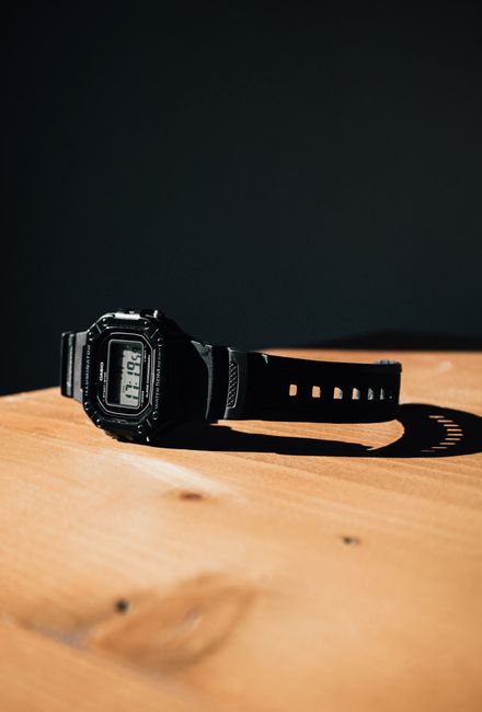 Minimalist photo of a black digital wristwatch on a wooden tabletop with shadow contrast.