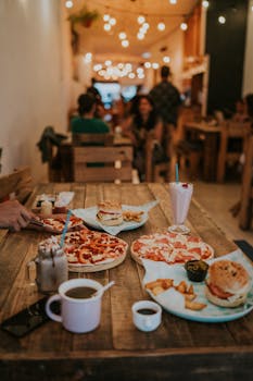 A warm restaurant setting with pizzas, burgers, and beverages on a rustic wooden table.