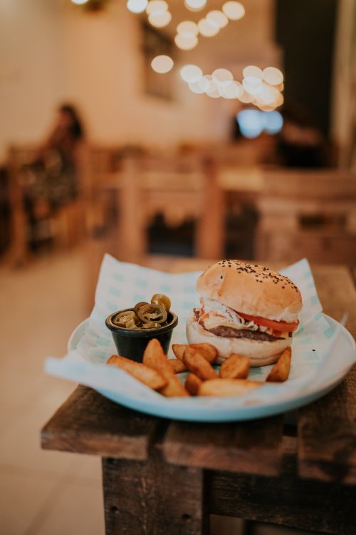 Free A mouth-watering burger with potato wedges served on a rustic table at a cozy cafe. Stock Photo