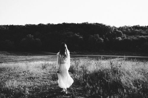 Free Black and white photo of a woman in a white dress walking through a serene field with trees. Stock Photo
