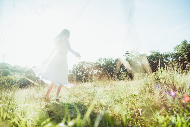 Woman In White Dress Walking On Green Grass Field