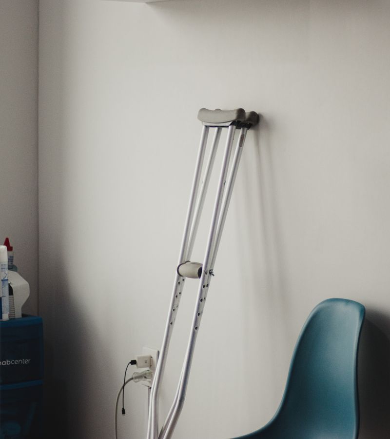 Crutches resting against a wall in a minimalist waiting room with blue chairs.