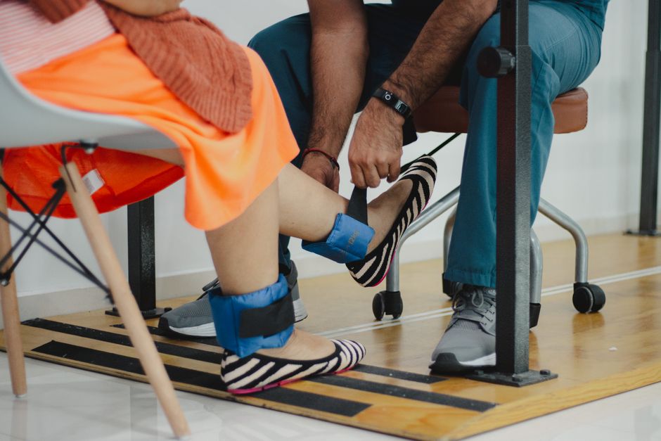 pexels photo 13185370 A therapist assists a woman during a rehabilitation session involving ankle weights.