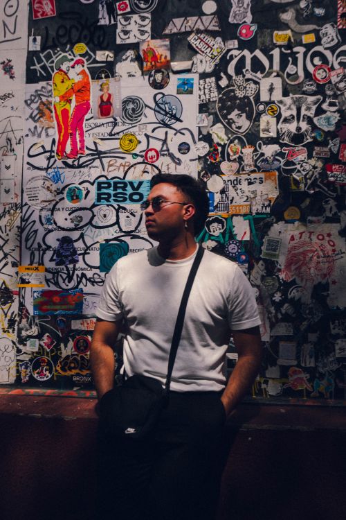 Free Trendy young man in sunglasses posing against a vibrant graffiti wall in an urban setting. Stock Photo