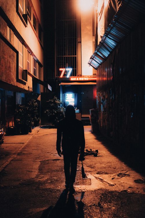 Free Dark urban alley at night featuring a silhouette and neon lights near bar entrance. Stock Photo