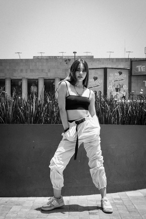 Free Black and white urban fashion shot featuring a woman in trendy streetwear posing confidently outdoors. Stock Photo