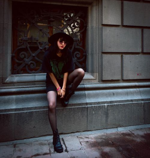 Free Stylish young woman in grunge outfit sitting on a stone ledge outdoors. Stock Photo