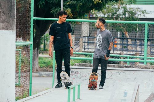 Free Two young men with tattoos conversing at an outdoor skate park. Stock Photo
