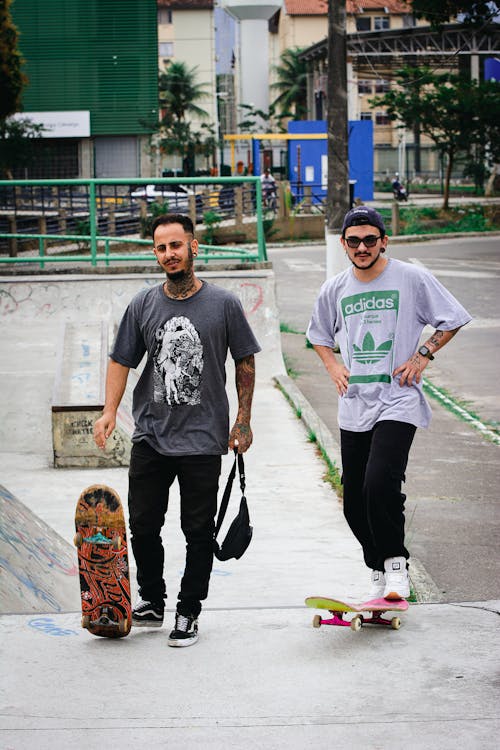 Man in White Crew Neck T-shirt and Black Pants Holding Orange and Yellow Skateboard