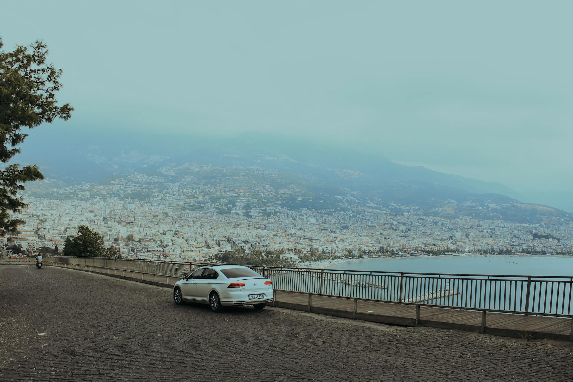 A white car on a cobblestone road with a stunning view of the coastal city and mountains in the background.