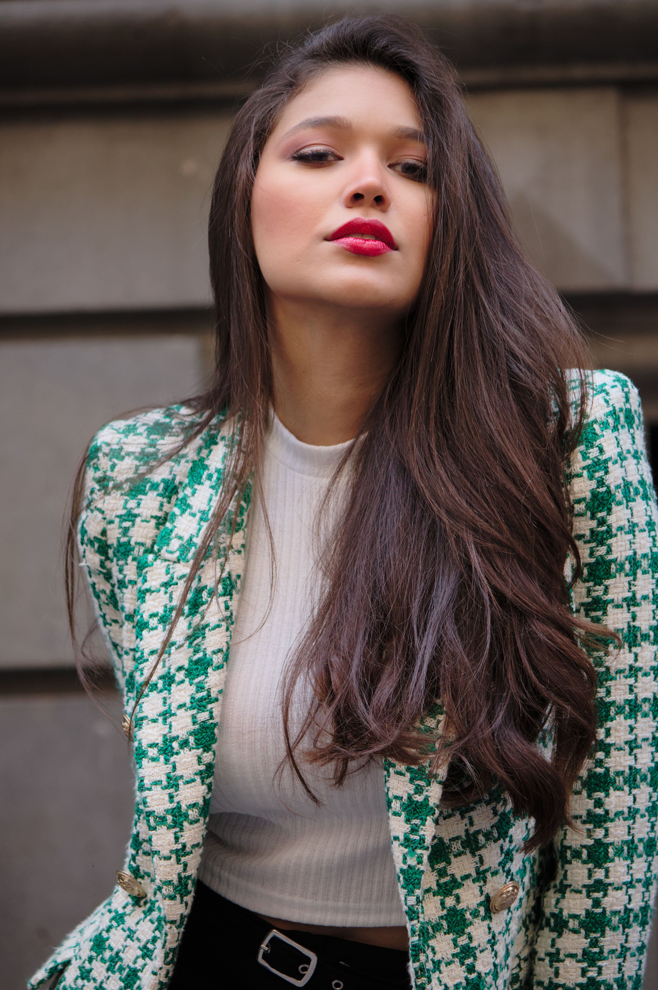 Stylish woman with long hair in a green plaid blazer posing confidently outdoors.