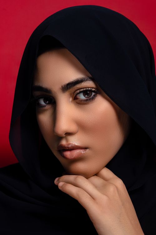 Free Close-up portrait of a woman wearing a hijab with a striking look against a red background. Stock Photo