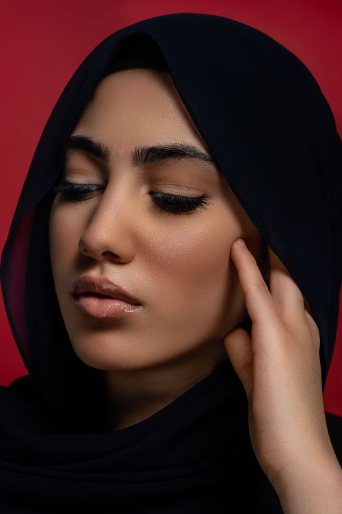 Free Close-up portrait of a woman in a hijab with eyes closed against a red background. Captures serenity and beauty. Stock Photo